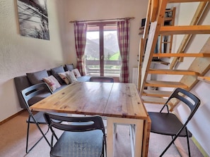 A dining area with a wooden table and chairs, a sofa with cushions, a window with curtains, and a wooden ladder. - Apartment with mezzanine and view - 5 guests (Méribel)