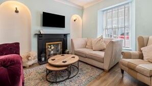 Ein Wohnzimmer mit Kamin, einer Couch, einem Sessel, einem Fernseher und einem gemusterten Teppich.