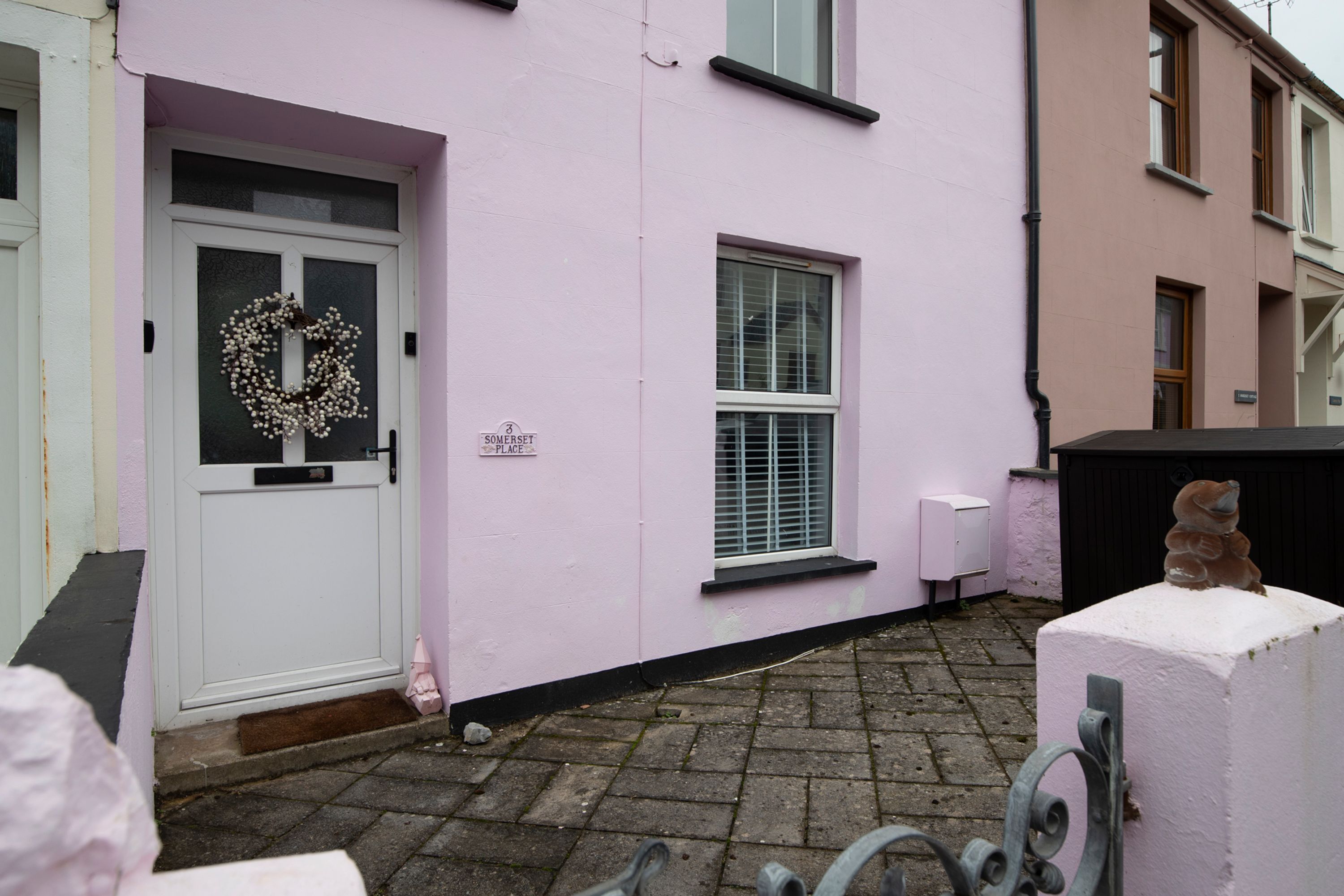 A pink building with a white door, a window, and a small outdoor area with a metal structure.