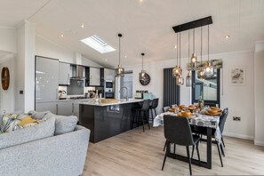 A modern kitchen with a central island, dining area with chairs, and a sofa. - Bryn Hafod - Luxury Lodge Hot Tub Walk to Beach (Tenby)