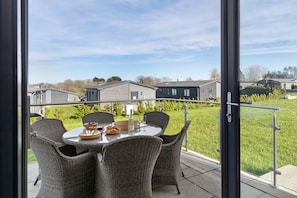 A balcony with wicker chairs and a table set for a meal, overlooking a residential area. - Bryn Hafod - Luxury Lodge Hot Tub Walk to Beach (Tenby)