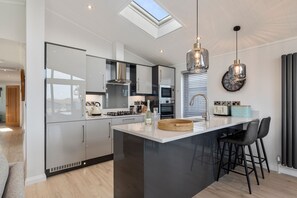 A modern kitchen with a skylight, a central island, and bar stools. - Bryn Hafod - Luxury Lodge Hot Tub Walk to Beach (Tenby)