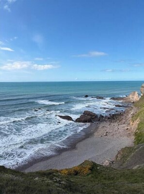 A coastal landscape with a beach, rocky shoreline, and ocean waves. - Sea View 3 Bed Apt, Moments to Beach, Sleeps 6 (Bude)