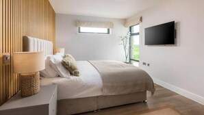 Een slaapkamer met een bed, een bedlampje, een televisie en een raam.