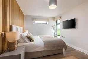 A bedroom with a bed, a bedside lamp, a TV, and a window. - Sea View Stylish Apt with Sauna, Steps to Beach (Bude)