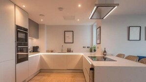 Een moderne keuken met ingebouwde apparatuur, een centraal eiland en een eethoek met stoelen.