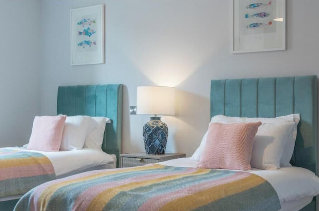 A hotel room with two beds, a nightstand with a lamp, and wall art.