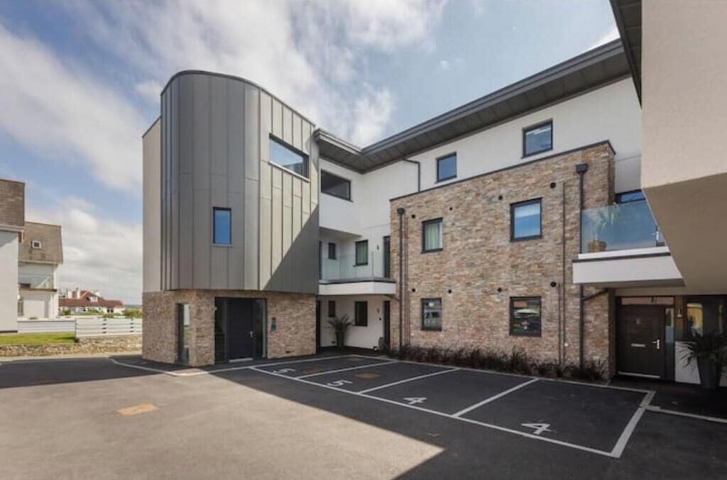 A modern building with a curved facade, a parking area, and a stone exterior.