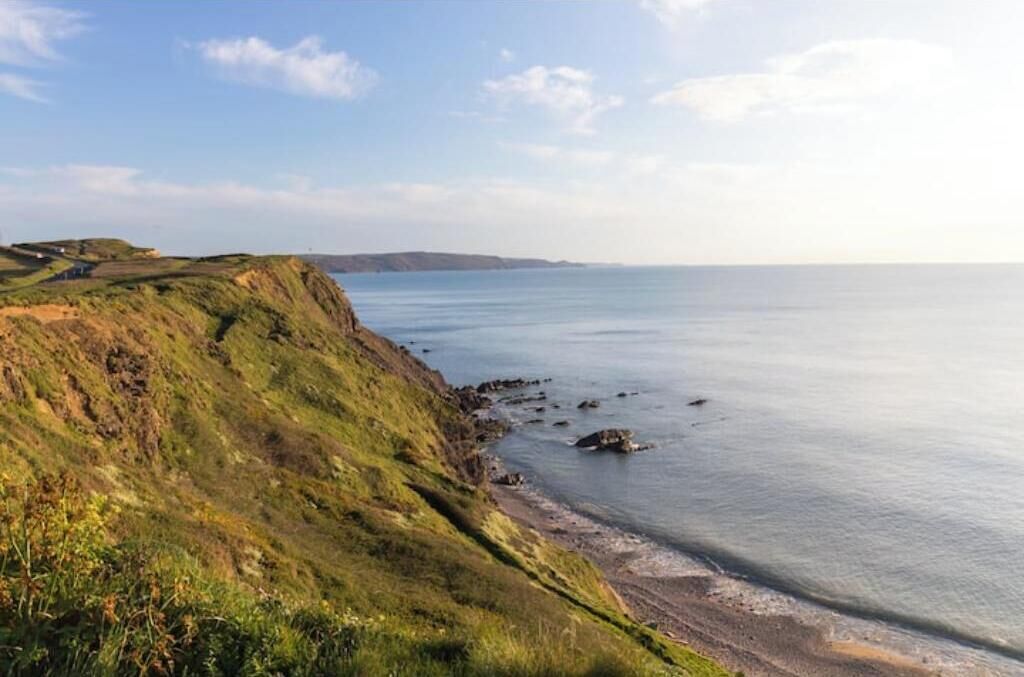 Un paysage côtier avec des falaises herbeuses et une mer calme.