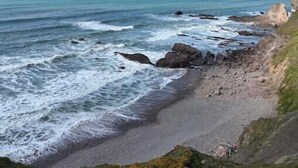 Een kustlandschap met een strand, een rotsachtige kustlijn en oceaan.