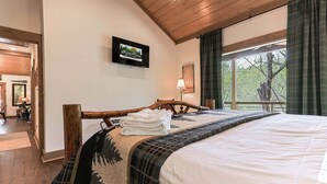 A bedroom with a wooden bed frame, a television on the wall, a window with curtains, and a view of trees outside. - Creekside Solace by Mountain Oasis | Near Aska Adventure Area w/Toccoa River Access (Blue Ridge)
