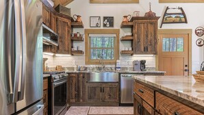 A kitchen with wooden cabinets, stainless steel appliances, and a window with a view of trees. - Creekside Solace by Mountain Oasis | Near Aska Adventure Area w/Toccoa River Access (Blue Ridge)