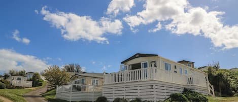 A two-story house with a balcony, a gravel driveway, and a clear sky.