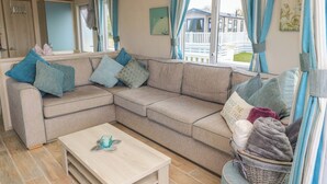 En hyggelig stue med en beige hjørnesofa, et træbord og udsigt til et hus gennem vinduerne.