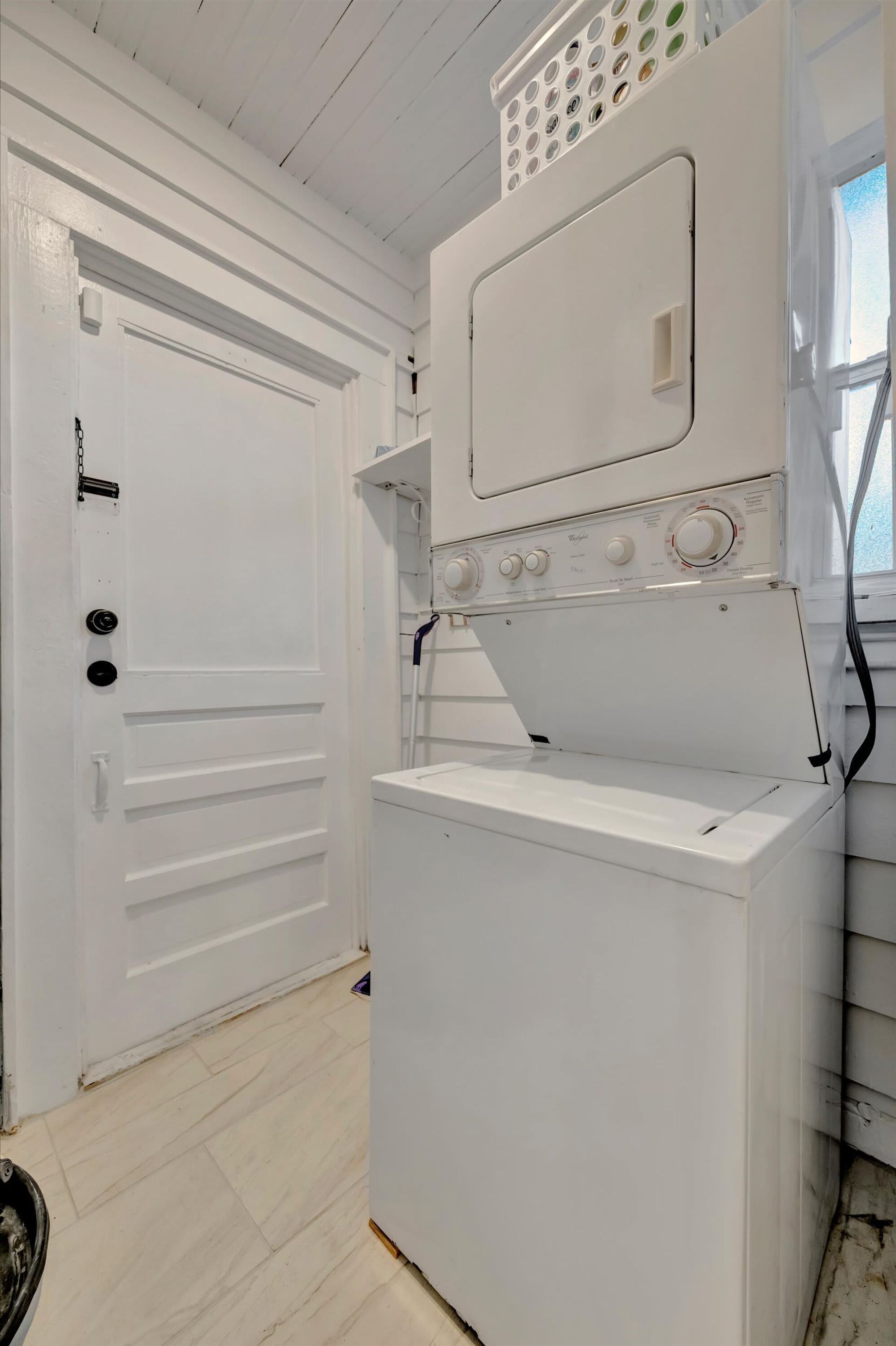 Een wasserette met een witte wasmachine, een deur en een raam.