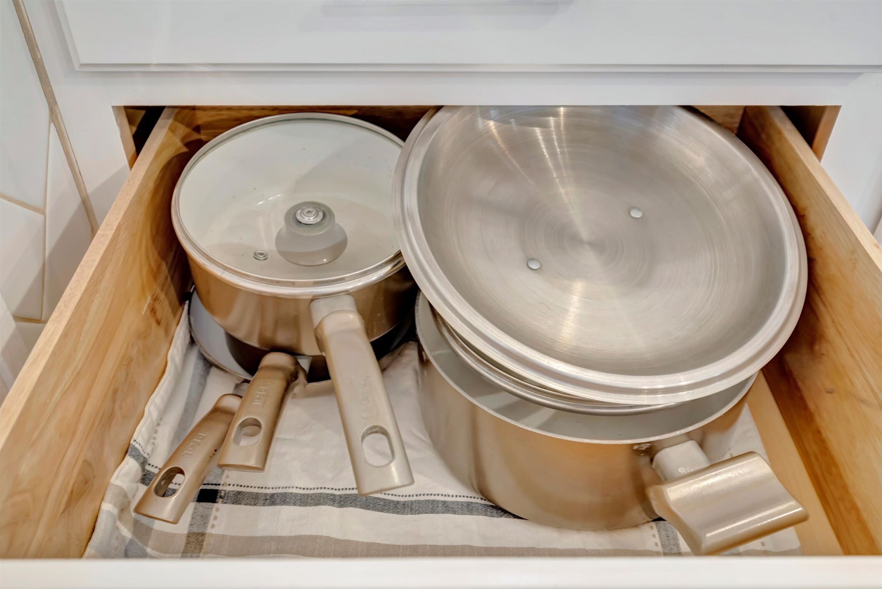 A kitchen drawer containing stainless steel cookware, including pots and pans with lids.