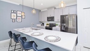 A modern kitchen with a large island, bar stools, pendant lighting, and stainless steel appliances. - 4BR Resort Home Pool Gym Disney Minutes Away (Davenport)