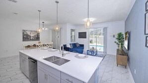 A modern kitchen with a large island, pendant lighting, and a blue sofa in the adjacent living area. - 4BR Resort Home Pool Gym Disney Minutes Away (Davenport)