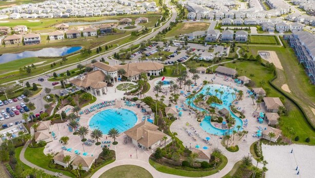 An aerial view of a resort with multiple swimming pools, a central pavilion, and a surrounding road. - 4BR Resort Home Pool Gym Disney Minutes Away (Davenport)