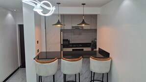 Una cocina moderna con encimera negra, tres taburetes de bar e iluminación colgante.