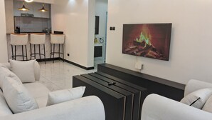 Una sala de estar moderna con chimenea, televisor y cocina al fondo.