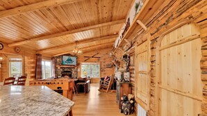 A log cabin interior with a stone fireplace, wooden dining table, and a mounted deer head. - Aspen Bear Retreat | Spa, Mountain Views, Near Bear Mountain & Slopes Sleeps 8 (Big Bear City)