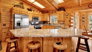 A wooden cabin kitchen with a central island, stainless steel appliances, and wooden stools. - Aspen Bear Retreat | Spa, Mountain Views, Near Bear Mountain & Slopes Sleeps 8 (Big Bear City)