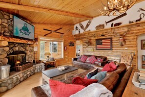 A rustic cabin interior with a stone fireplace, wooden walls, a leather sofa, and a mounted American flag.