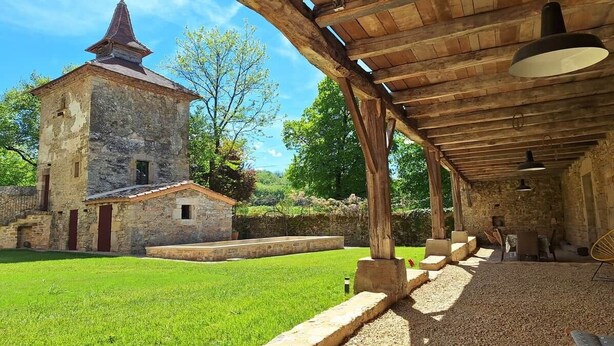 A stone building with a conical roof, a covered outdoor area with seating, and a grassy courtyard. - Gîte le pigeonnier de la jalberterie (Varen)