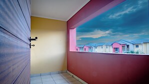 A room with a tiled floor, a wooden door, a yellow wall, and a red wall with a view of houses.