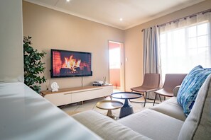 Een moderne woonkamer met een flatscreen televisie, een bank, twee bijzettafeltjes, een potplant en uitzicht op de omgeving.