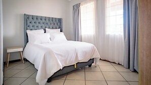 A neatly made bed with white bedding, a tufted headboard, and a bedside table with a drawer.