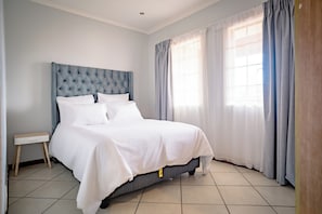 Een opgemaakt bed met witte lakens, een gestoffeerd hoofdbord en een nachtkastje met een lade.