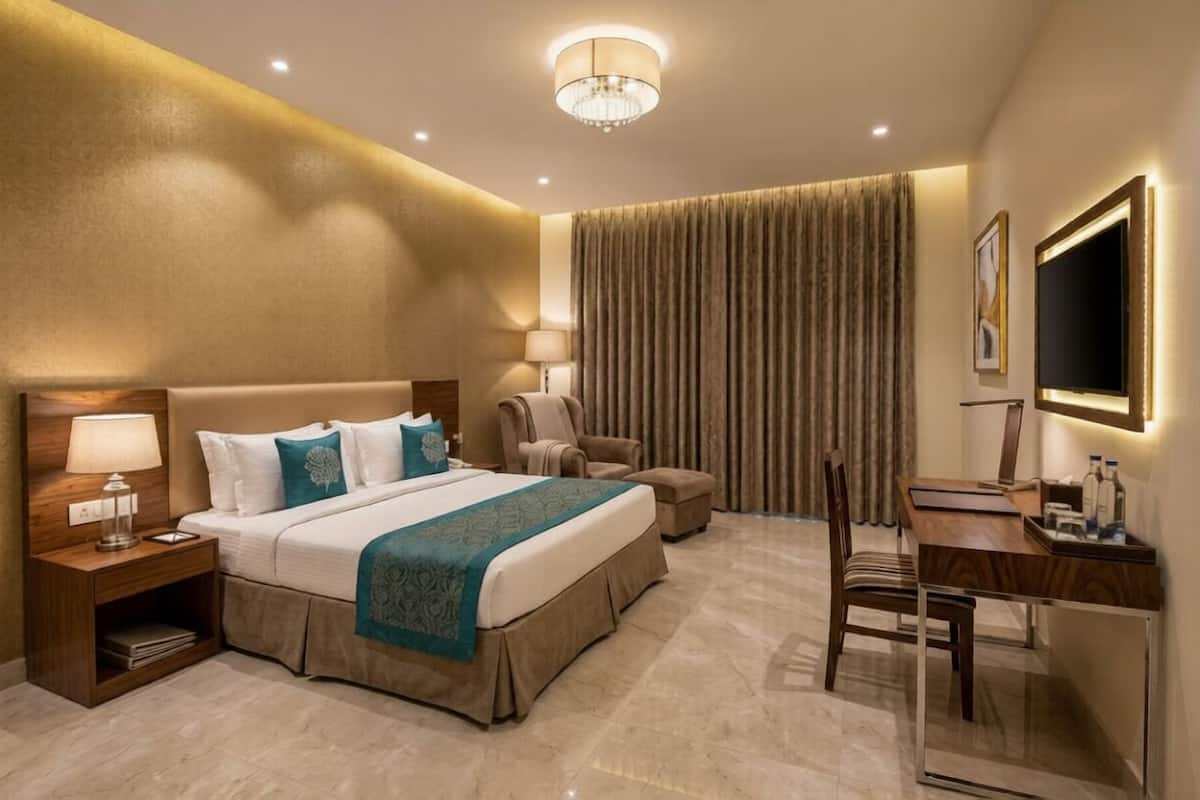 A hotel room with a bed, a desk, a chair, a lamp, and a television.