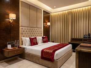 A hotel room with a large bed, a wooden nightstand, a desk, and a wall-mounted lamp. - HOTEL THE MIRAGE (Ludhiana)