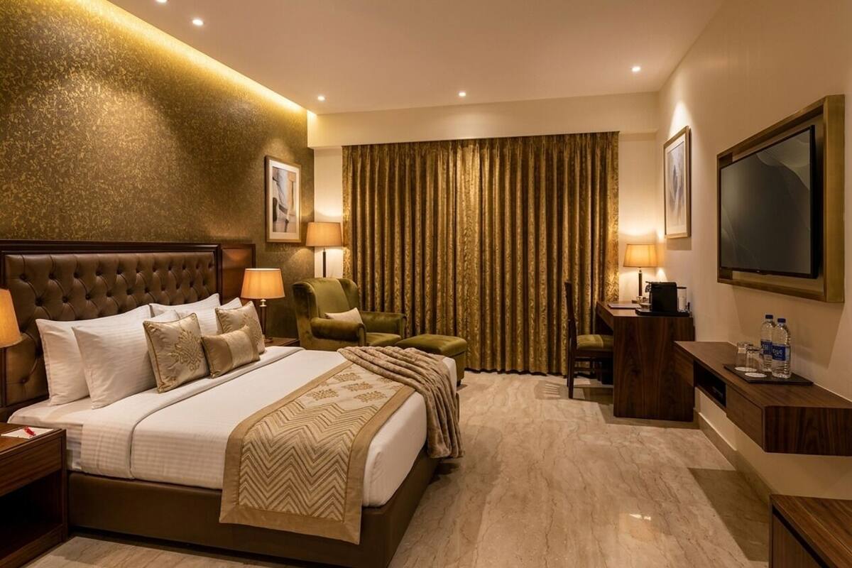 A hotel room with a large bed, a desk, a chair, a television, and a curtain.