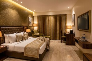 Una habitación de hotel con una cama grande, un escritorio, una silla, un televisor y una cortina.
