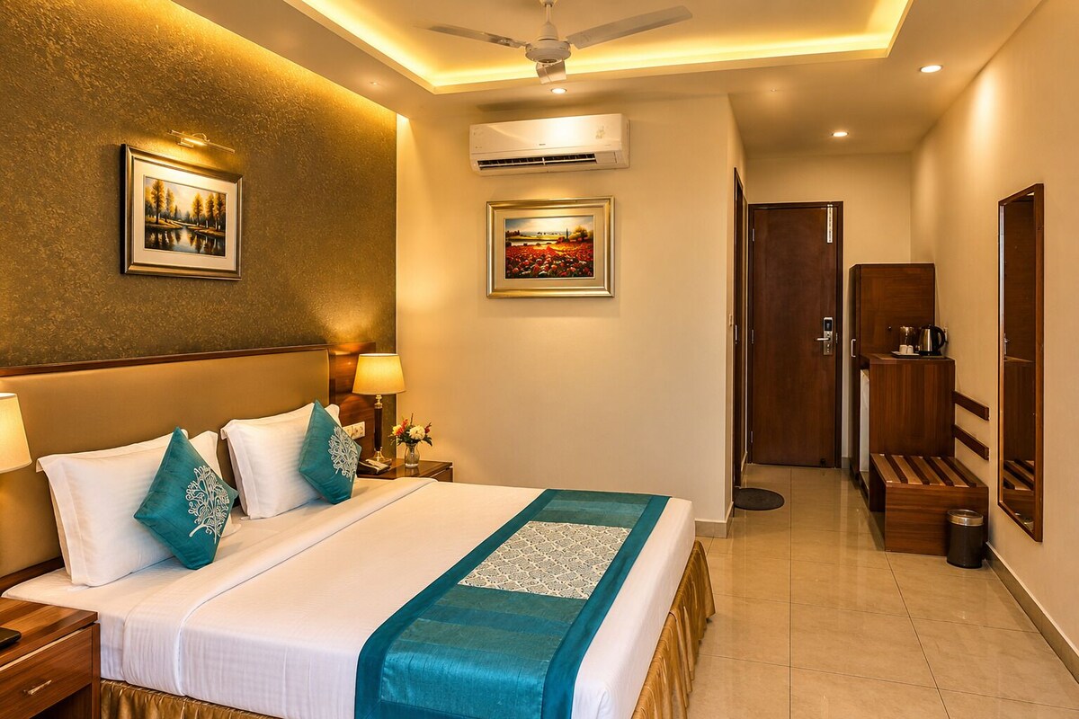 Habitación de hotel con cama, mesitas de noche, lámpara, aire acondicionado, ventilador de techo, puerta y banco.