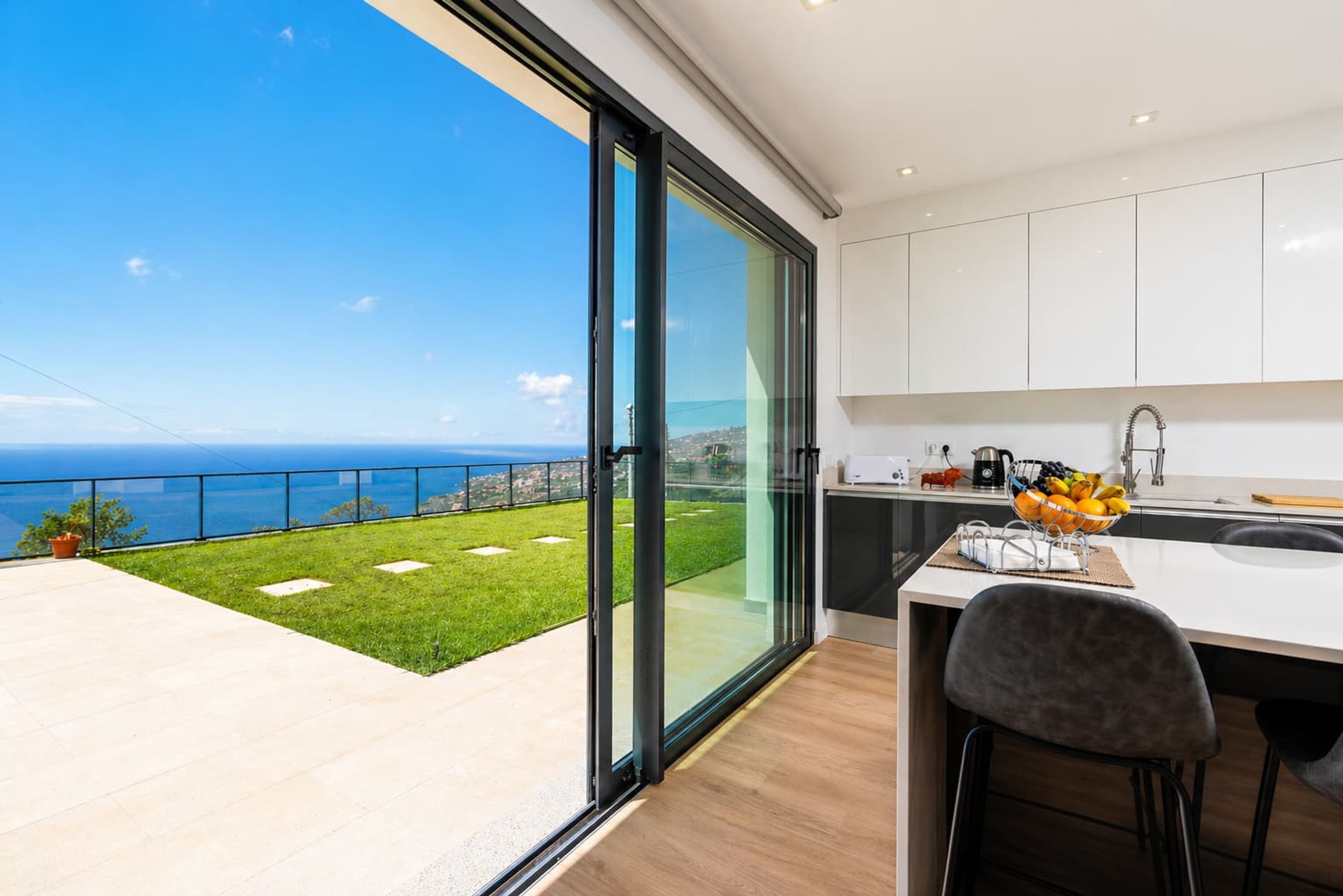 Eine moderne Küche mit einem großen Fenster mit Blick auf eine Wiese und das Meer.