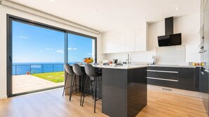 Uma cozinha moderna com uma ilha grande, banquetas e vista para o oceano.