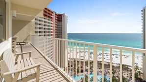 Ein Balkon mit Blick auf Strand und Meer, ein Pool und ein mehrstöckiges Gebäude mit Balkonen.