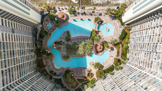 Ein Hochhaus-Hotel mit mehreren Balkonen, einem zentral gelegenen Pool und umgebender Bepflanzung.