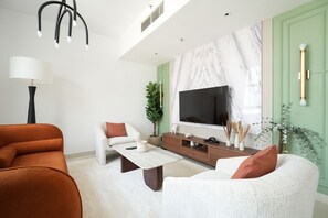 A modern living room with a sofa, coffee table, TV, and decorative plants. - Gala Guests - Standpoint Residences (Dubai)