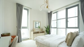 Ein Schlafzimmer mit Bett, Schreibtisch, Kommode und großen Fenstern.