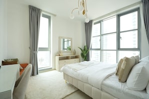 A bedroom with a bed, a desk, a dresser, and large windows. - Gala Guests - Standpoint Residences (Dubai)