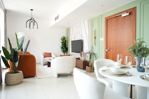 Uma sala de estar moderna com sofá, poltronas, mesa de jantar posta com pratos e copos, televisão e uma grande porta de madeira.