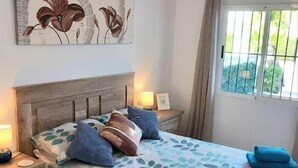 A bedroom with a bed, nightstands, a ceiling fan, a window with curtains, and a wall painting.
