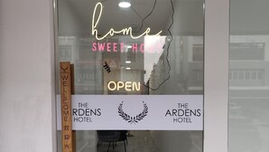 Ein Hotel Eingang mit Glastür, einem Neon-Schild mit der Aufschrift 'home SWEET-HOME' und einem Willkommensschild.