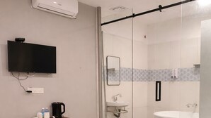 Ein Hotelzimmer mit einem Bett, einem Fernseher, einem Schreibtisch mit Kaffeemaschine, einem Spiegel, einem Waschbecken und einer Badewanne.