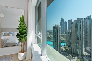 Ein modernes Schlafzimmer mit großem Fenster, einem Blumentopf, einem Bett mit gemusterten Kissen und Blick auf die Stadt.